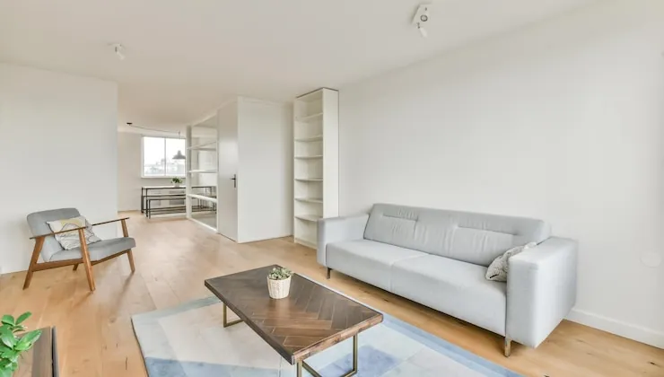 A bright living room in a renovated flat, with a grey sofa, oak parquet flooring and white walls