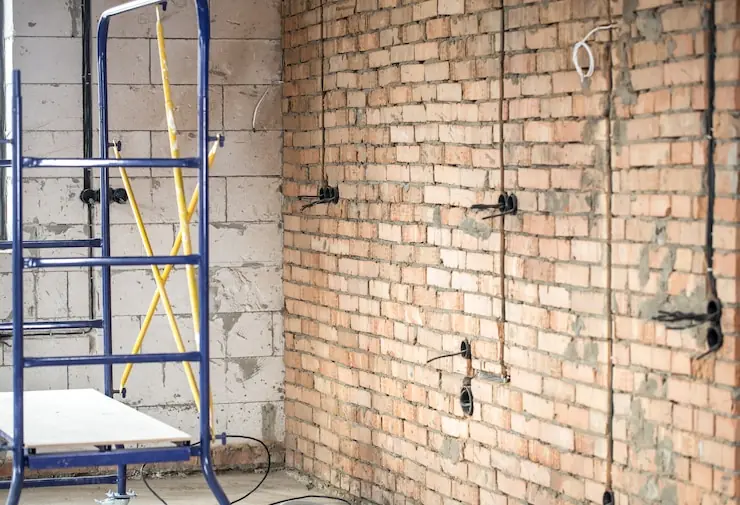 A brick wall with new electrical wiring and scaffolding in a flat under renovation
