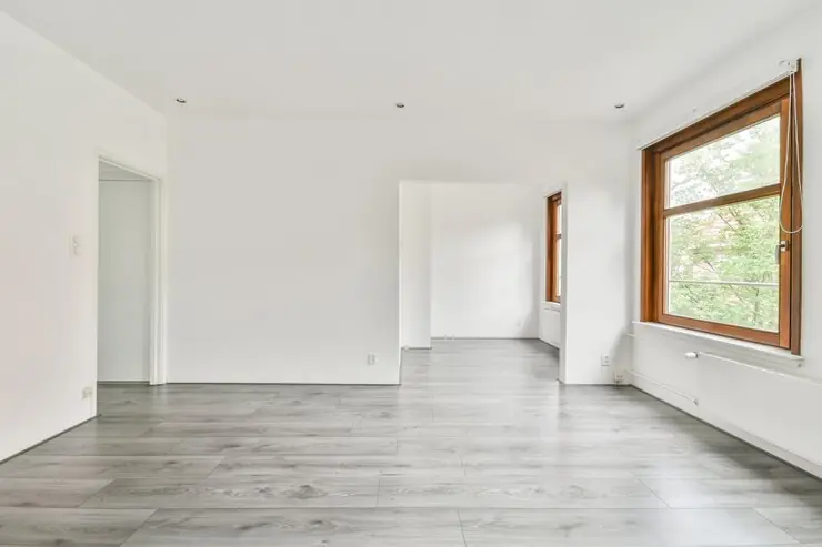 An empty room with smooth white walls and grey laminate flooring, ready for furniture